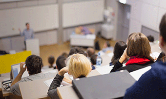 Students in a lecture hall facing a professor giving a lecture