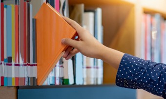 A person selecting a book from a shelf lined with various literature