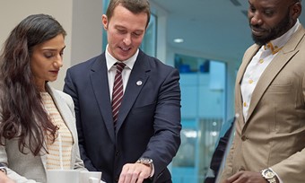 A diverse group of professionals in business attire collaborating around a laptop