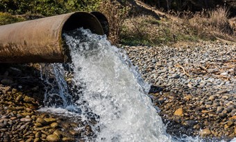 Rusted metal pipe with water flowing out the end into a riverbed