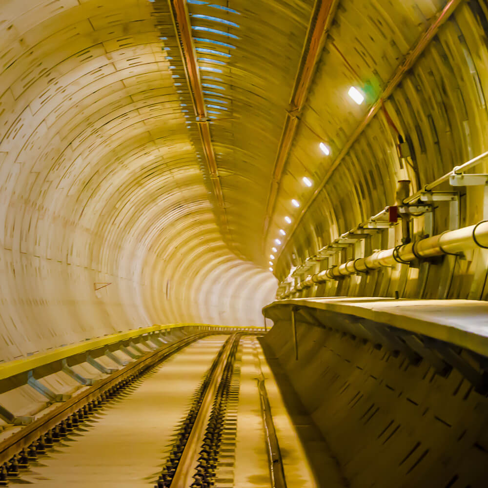 Train tracks entering a bend inside the corner of a well lit underground tunnel