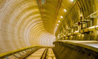 Train tracks entering a bend inside the corner of a well lit underground tunnel