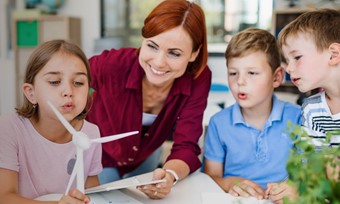 Children and a teacher study a handheld model of a wind turbine together