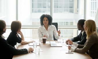 A woman speaks to her colleagues at a conference table