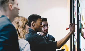 Group of individuals examining a board covered in colorful sticky notes.