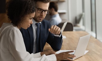 A man and woman in business attire looking at a laptop screen.